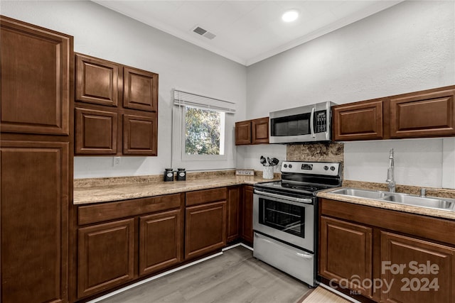 kitchen with stainless steel appliances, light hardwood / wood-style flooring, ornamental molding, and sink