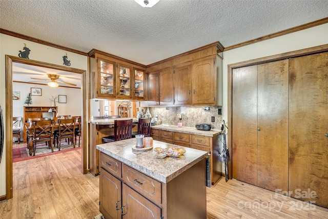 kitchen with ceiling fan, light hardwood / wood-style floors, a textured ceiling, tasteful backsplash, and a kitchen island