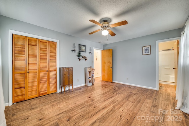 unfurnished bedroom featuring ceiling fan, ensuite bathroom, light hardwood / wood-style floors, a textured ceiling, and a closet