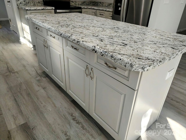 kitchen featuring hardwood / wood-style flooring, light stone countertops, a kitchen island, white cabinetry, and stainless steel appliances