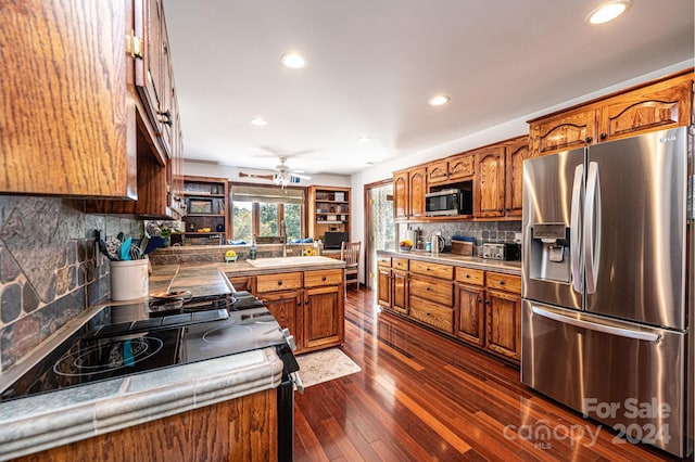 kitchen with ceiling fan, dark hardwood / wood-style flooring, appliances with stainless steel finishes, and tasteful backsplash