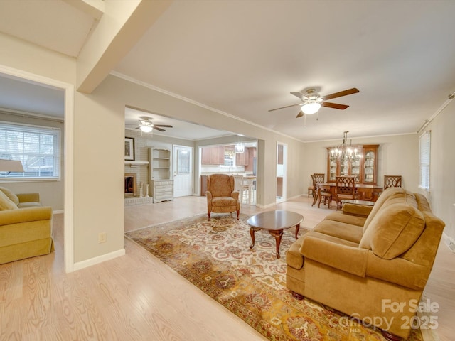 living room with built in features, crown molding, a fireplace, ceiling fan with notable chandelier, and light wood-type flooring