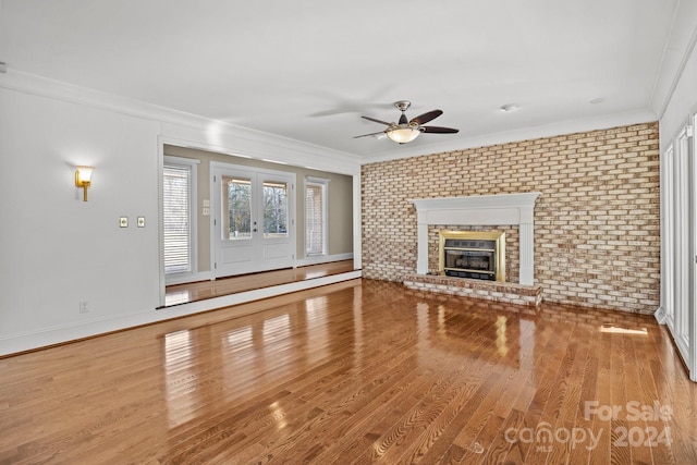 unfurnished living room with ceiling fan, a brick fireplace, brick wall, hardwood / wood-style floors, and ornamental molding