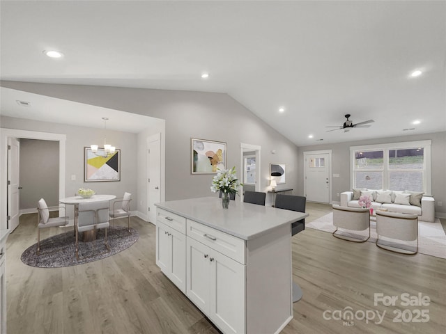 kitchen featuring pendant lighting, lofted ceiling, light hardwood / wood-style floors, white cabinets, and ceiling fan with notable chandelier