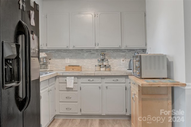 kitchen with decorative backsplash, black fridge with ice dispenser, light hardwood / wood-style flooring, and white cabinetry