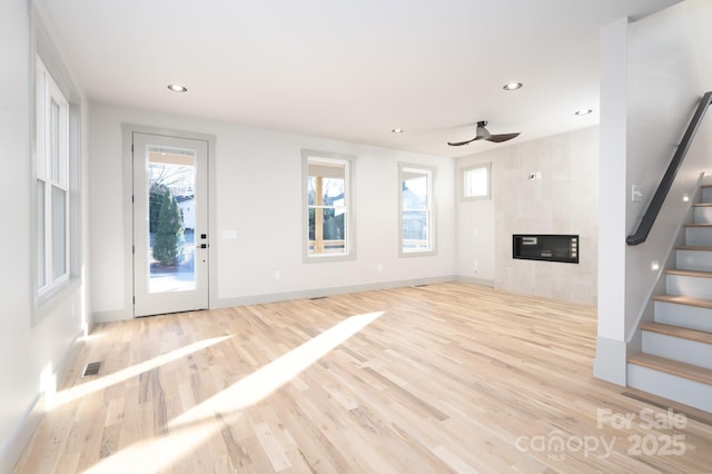 unfurnished living room with light hardwood / wood-style flooring, ceiling fan, and a tiled fireplace