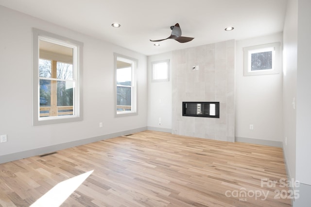 unfurnished living room featuring ceiling fan, light hardwood / wood-style flooring, plenty of natural light, and a tiled fireplace