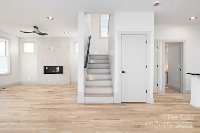 stairs with a wealth of natural light, ceiling fan, a fireplace, and wood-type flooring