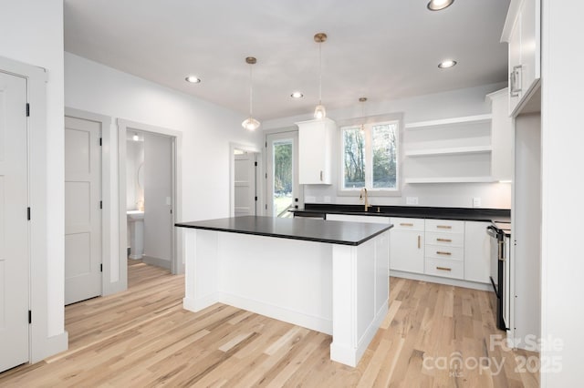 kitchen with black range with electric cooktop, sink, white cabinets, a kitchen island, and hanging light fixtures