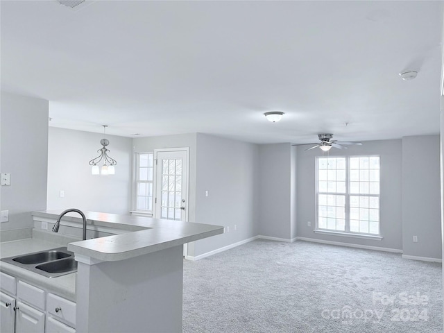 kitchen with ceiling fan, sink, hanging light fixtures, light colored carpet, and white cabinets