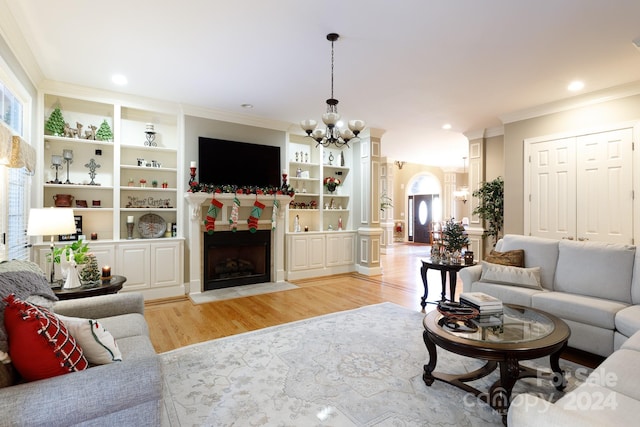 living room featuring an inviting chandelier, ornamental molding, built in features, and light hardwood / wood-style flooring