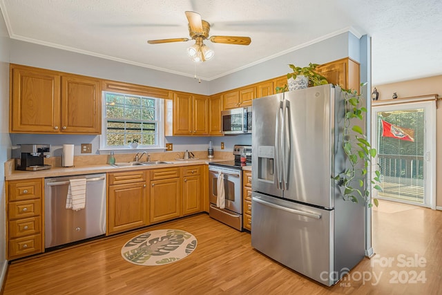 kitchen featuring sink, light hardwood / wood-style flooring, ornamental molding, a textured ceiling, and appliances with stainless steel finishes