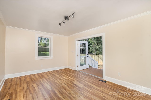 empty room featuring track lighting, light hardwood / wood-style flooring, and ornamental molding