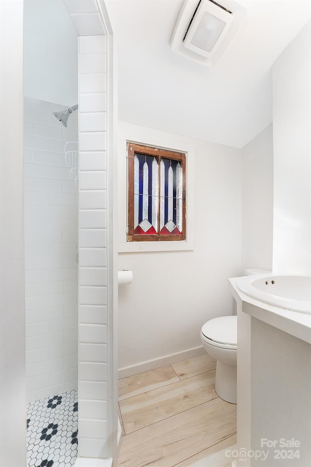 bathroom with hardwood / wood-style floors, toilet, and tiled shower