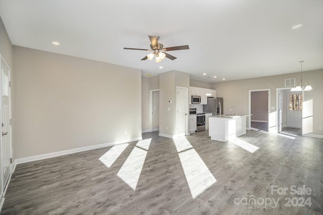 unfurnished living room with wood-type flooring, ceiling fan with notable chandelier, and sink