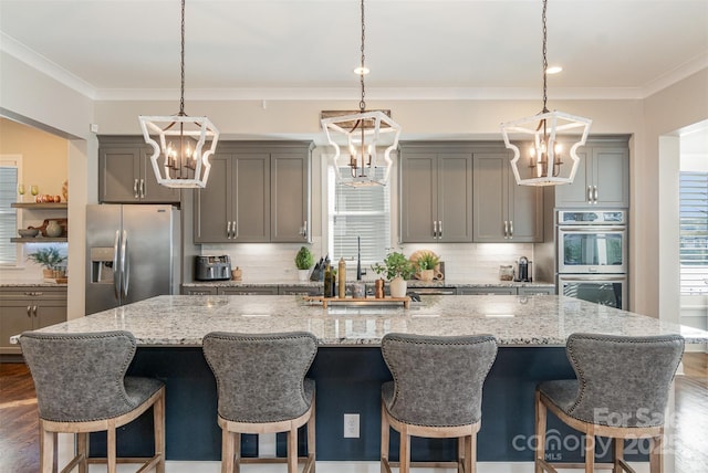 kitchen with appliances with stainless steel finishes, a kitchen breakfast bar, a large island with sink, decorative light fixtures, and a chandelier