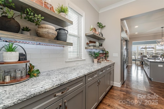 bar featuring tasteful backsplash, crown molding, decorative light fixtures, stainless steel refrigerator, and light stone countertops