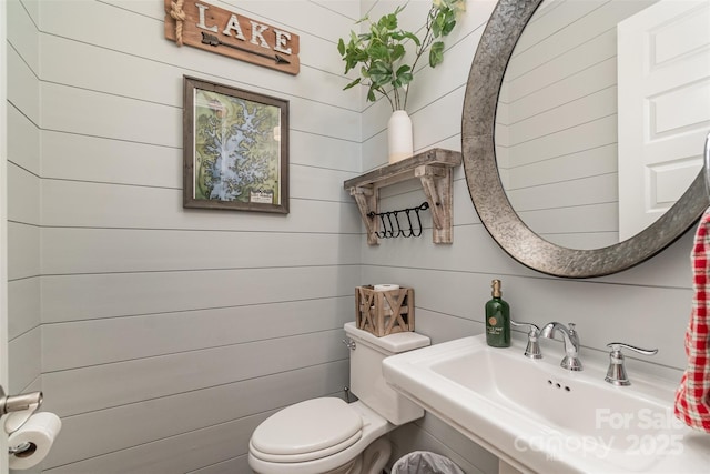 bathroom featuring toilet, sink, and wood walls