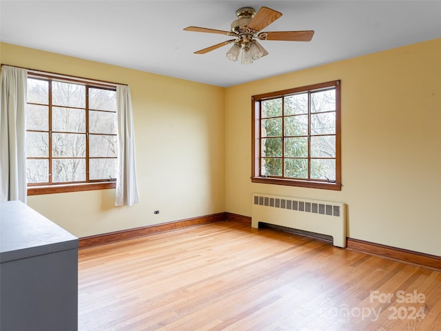 unfurnished room with ceiling fan, a healthy amount of sunlight, radiator heating unit, and light hardwood / wood-style flooring