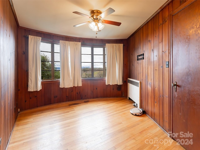 unfurnished room featuring light wood-type flooring, ornamental molding, ceiling fan, wooden walls, and radiator heating unit