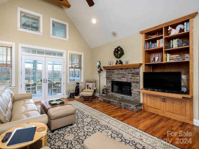 living room with ceiling fan, french doors, a stone fireplace, high vaulted ceiling, and hardwood / wood-style flooring