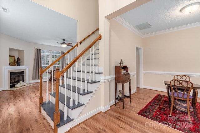 stairs featuring a textured ceiling, hardwood / wood-style flooring, ceiling fan, and ornamental molding