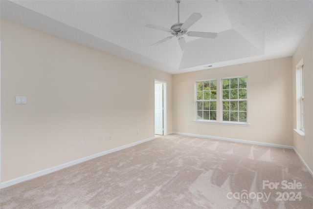 empty room with a textured ceiling, light colored carpet, ceiling fan, and a tray ceiling