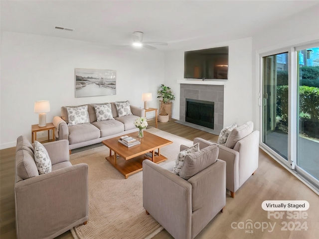 living room with ceiling fan, light wood-type flooring, and a tiled fireplace