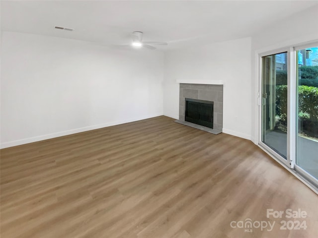 unfurnished living room featuring hardwood / wood-style flooring, ceiling fan, and a tiled fireplace