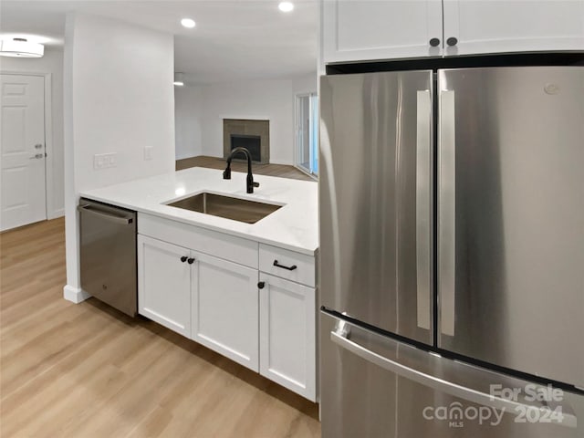 kitchen featuring a fireplace, stainless steel appliances, sink, light hardwood / wood-style flooring, and white cabinets