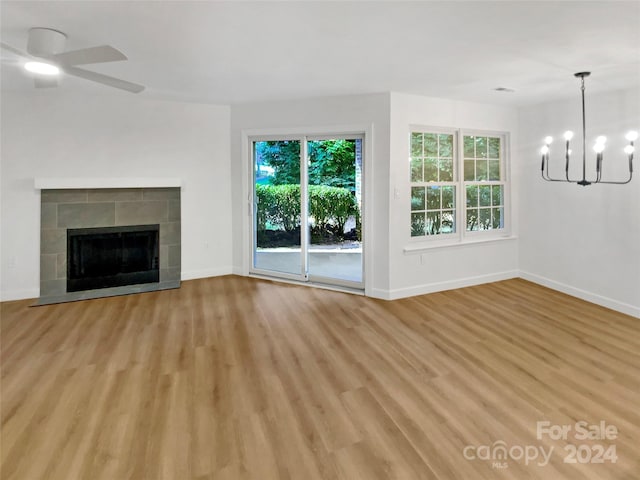 unfurnished living room with ceiling fan with notable chandelier, light wood-type flooring, and a tiled fireplace