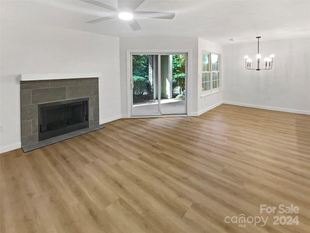 unfurnished living room with a fireplace, ceiling fan with notable chandelier, and light hardwood / wood-style floors