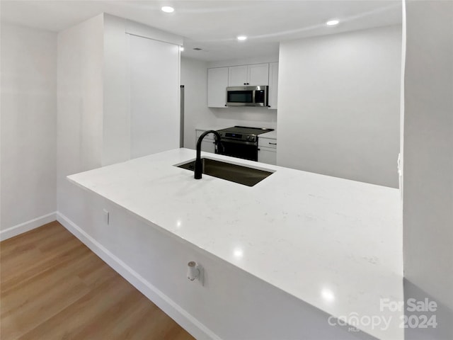 kitchen with black range with electric stovetop, sink, white cabinets, and light wood-type flooring