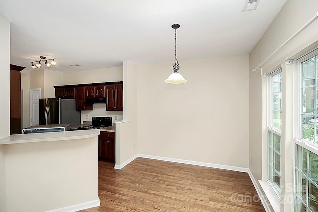 kitchen featuring black range oven, dark brown cabinets, decorative light fixtures, light hardwood / wood-style floors, and stainless steel refrigerator