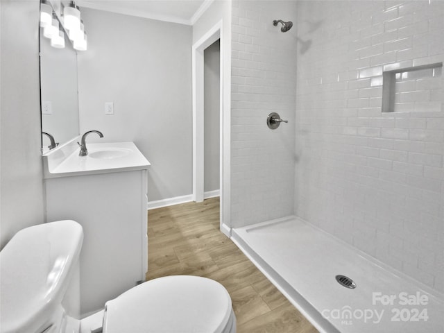 bathroom with vanity, crown molding, hardwood / wood-style flooring, toilet, and a tile shower