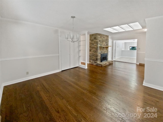 unfurnished living room featuring crown molding, a stone fireplace, dark wood-type flooring, and an inviting chandelier