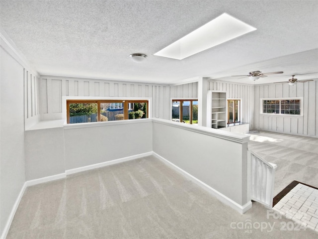 carpeted empty room with plenty of natural light, ceiling fan, a textured ceiling, and a skylight