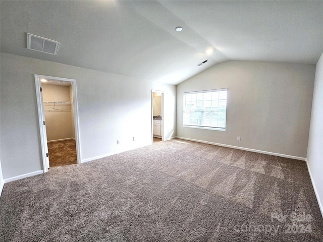 unfurnished bedroom with ensuite bath, carpet floors, lofted ceiling, a walk in closet, and a closet