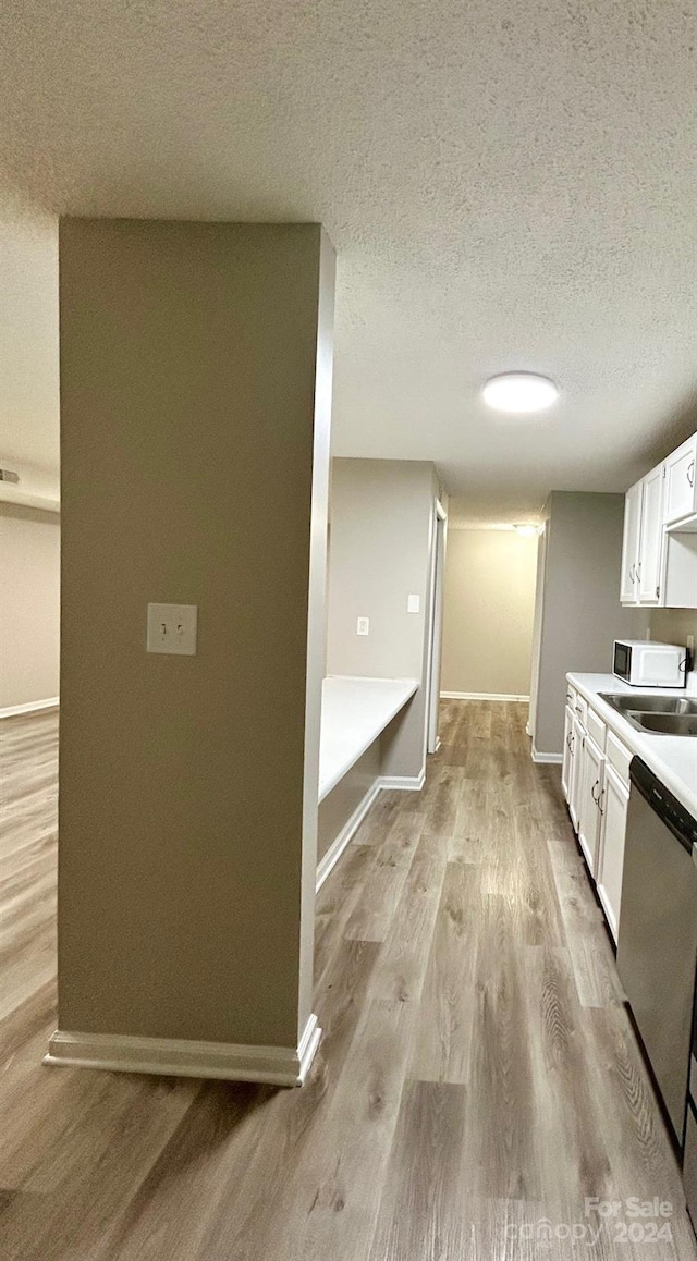 kitchen featuring dishwasher, a textured ceiling, light wood-type flooring, and white cabinetry