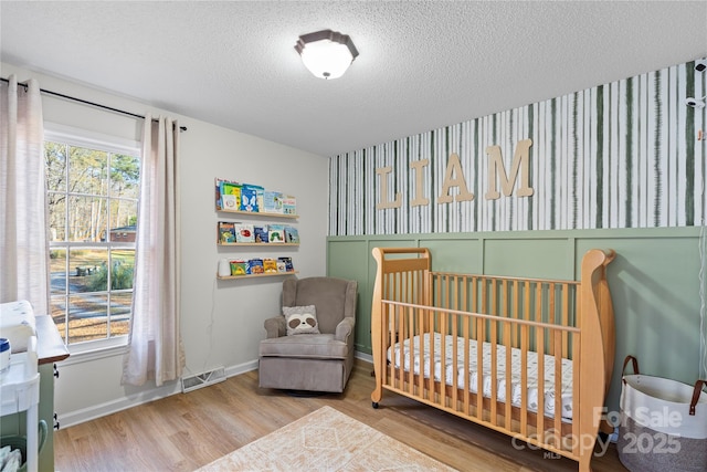 bedroom featuring multiple windows, a textured ceiling, a nursery area, and light wood-type flooring