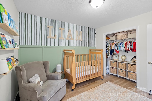 bedroom featuring a closet, a crib, a textured ceiling, and hardwood / wood-style flooring