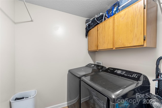 clothes washing area featuring cabinets, a textured ceiling, and washer and clothes dryer