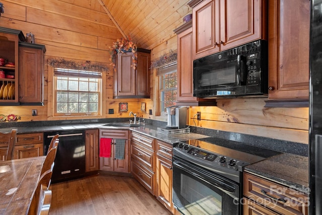 kitchen featuring sink, vaulted ceiling, wood walls, and black appliances