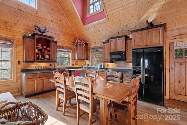 kitchen with light hardwood / wood-style flooring, high vaulted ceiling, wood walls, and black appliances