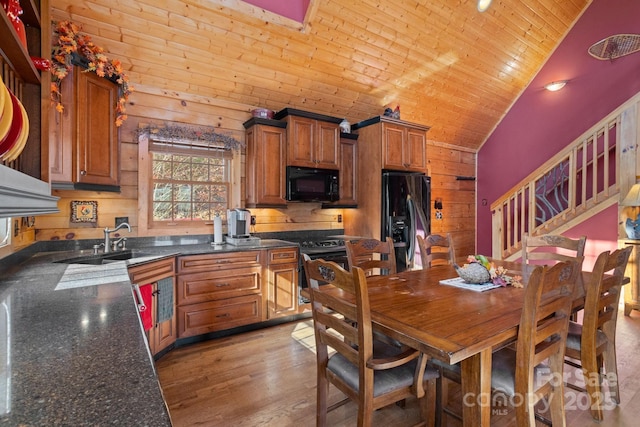 kitchen featuring high vaulted ceiling, black appliances, sink, wooden walls, and light wood-type flooring