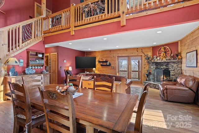 dining room featuring wood-type flooring, a stone fireplace, a high ceiling, and wood walls