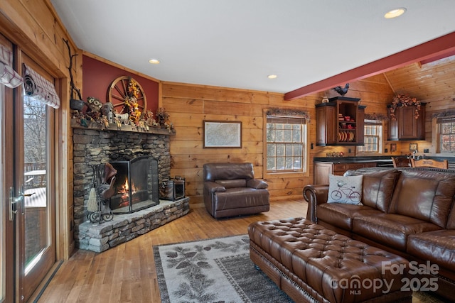 living room featuring a stone fireplace, light wood-type flooring, wooden walls, and vaulted ceiling