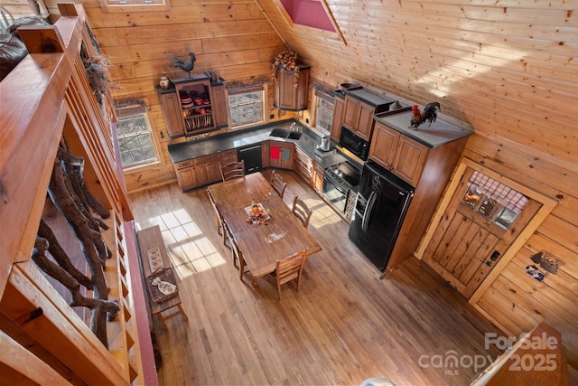 kitchen featuring wooden walls, dishwasher, high vaulted ceiling, and light hardwood / wood-style floors