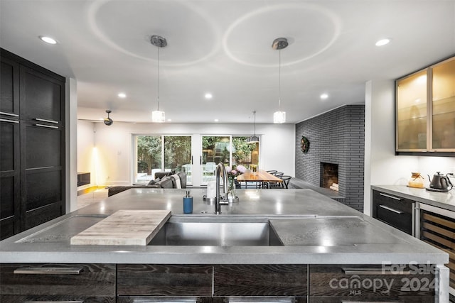 kitchen with a fireplace, wine cooler, hanging light fixtures, and a kitchen island with sink