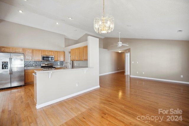 kitchen with appliances with stainless steel finishes, a kitchen breakfast bar, ceiling fan with notable chandelier, pendant lighting, and light hardwood / wood-style flooring